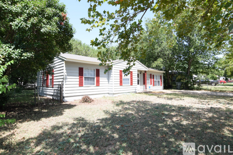 A small house with red trim is surrounded by trees.