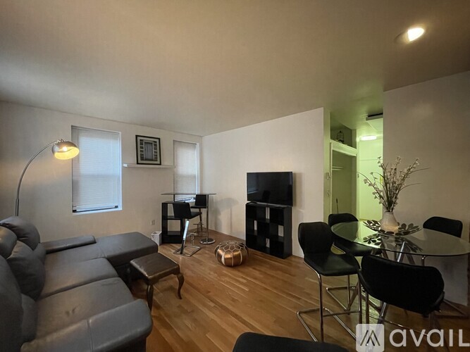 A living room with a black leather couch, a glass table, and a television.