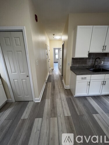 A hallway with a white door and a kitchen area with white cabinets.