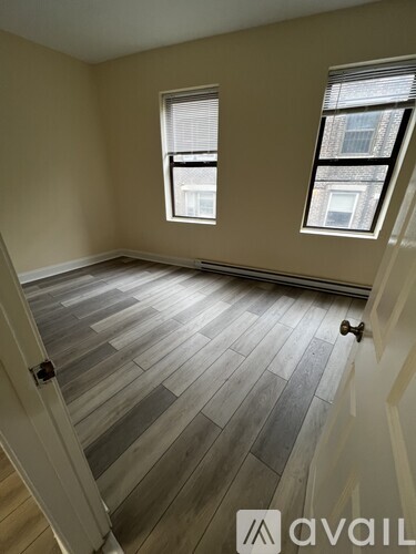 A room with wooden flooring and two windows.