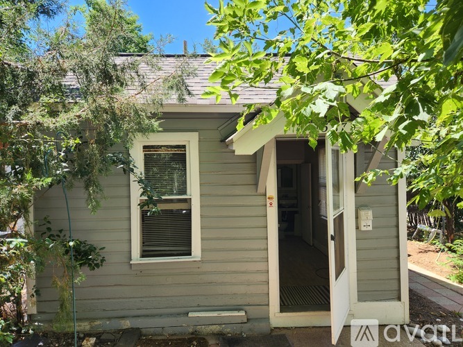 A small house with a door and window is surrounded by greenery.