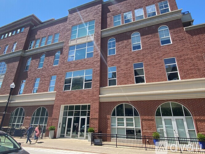 A red brick building with large windows and a black fence in front.