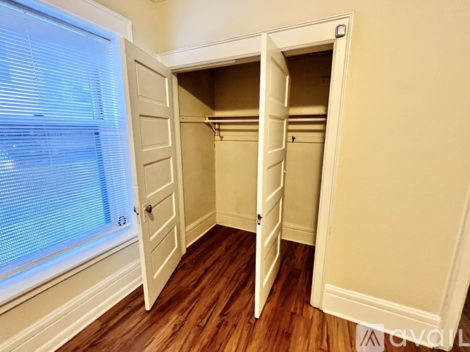 A white closet with a door open and a window with blinds to the left.
