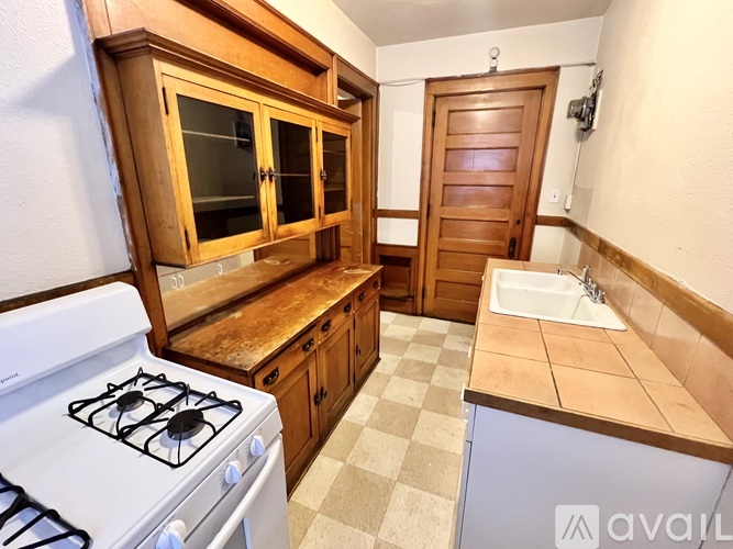 A kitchen with a white gas stove, wooden cabinets, and a checkered floor.