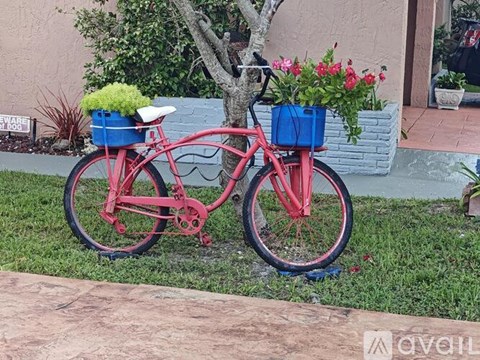 A red bicycle with a basket full of flowers is parked by a tree.