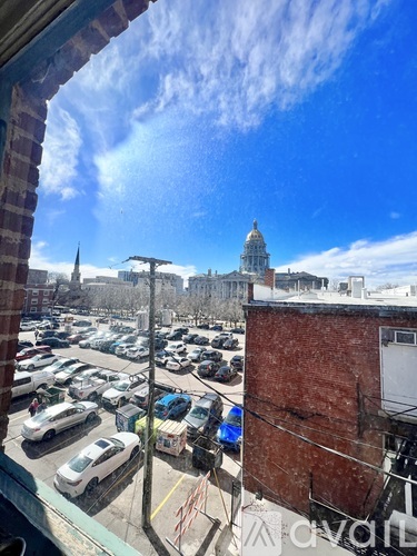 A view from a window of a parking lot with cars and a building in the distance.