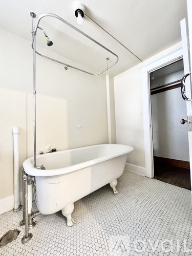 A white claw foot tub sits in a bathroom with a shower head above it.