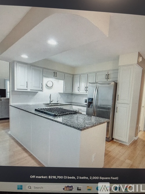 A kitchen with white cabinets and a black countertop is on the market for $210,700.