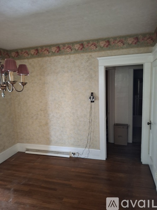 A room with a wooden floor and a wallpapered wall with a floral border.