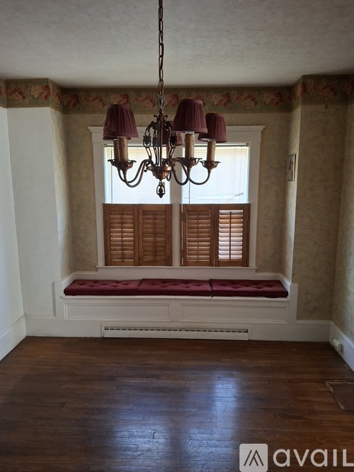 A room with a window, wooden bench and a chandelier.