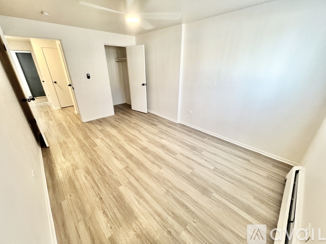 A spacious room with light wood flooring and white walls.