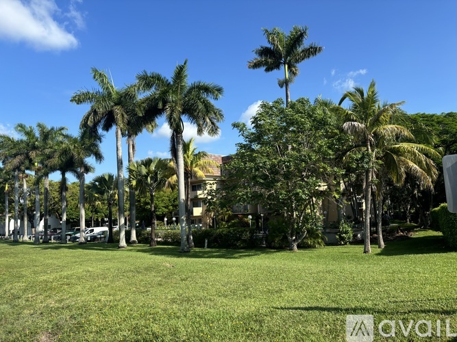 A grassy area with palm trees and a building in the background.