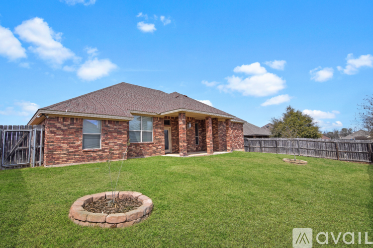 A house with a brown roof and a brick exterior is surrounded by a green lawn and a wooden fence.