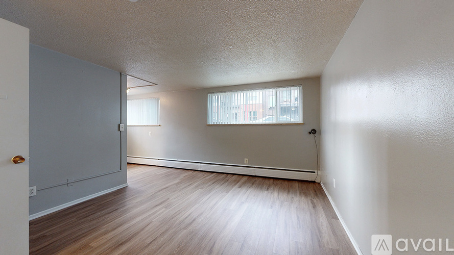 A room with wooden flooring and white walls, with a window and a door visible.