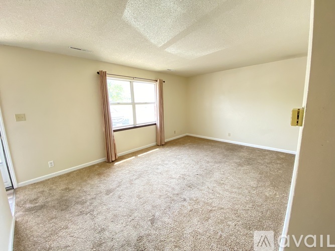 A room with a carpeted floor and a window with curtains.