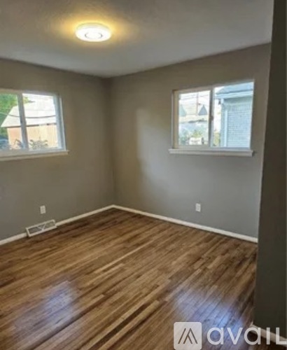 A room with wooden flooring and two windows.