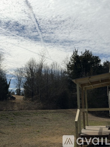 A wooden structure sits in a field with trees in the background.