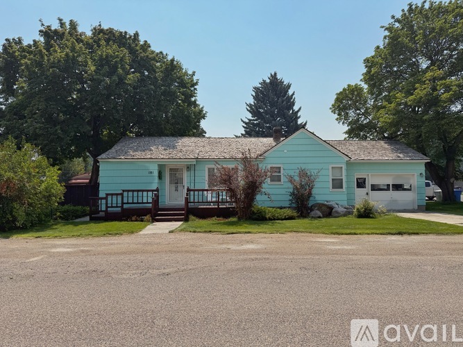 A blue house with a white garage door and a tree in front of it.