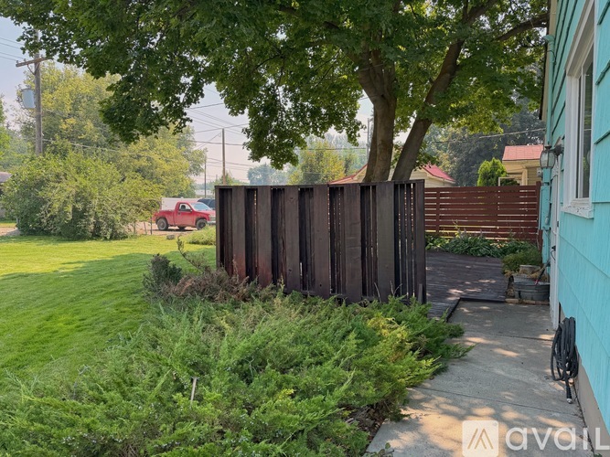 A red car is parked in a yard behind a wooden fence.