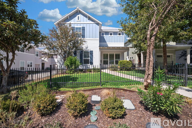 A house with a white and grey exterior is surrounded by a black fence and has a garden in front.