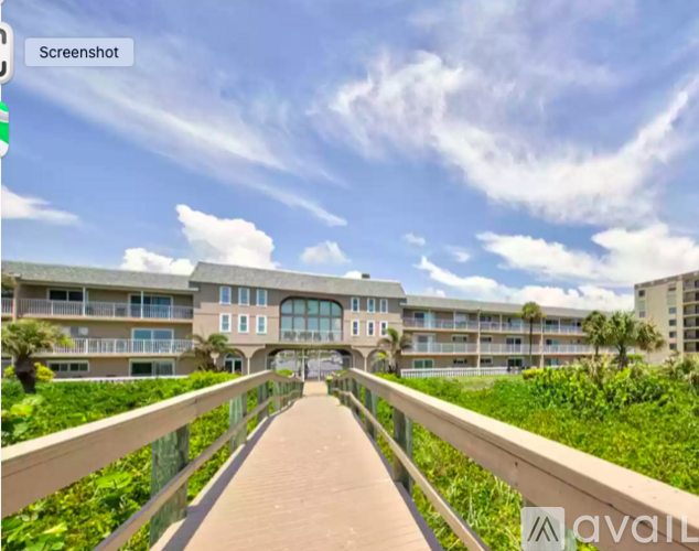 A walkway leads to a building with a balcony and a railing.