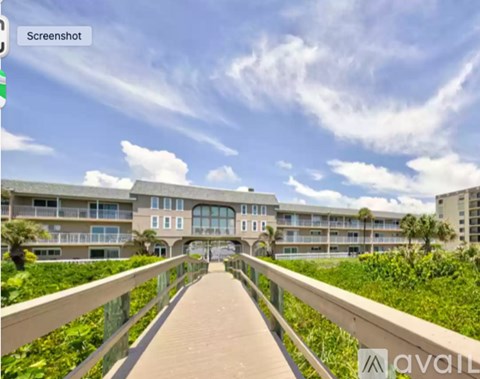 A walkway leads to a building with a balcony and a railing.