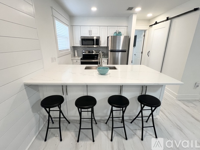 A kitchen with white cabinets and a white island with black stools.