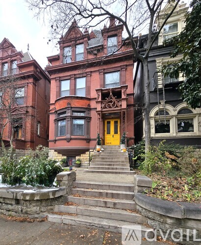 A red Victorian style house with a yellow door and steps leading up to it.