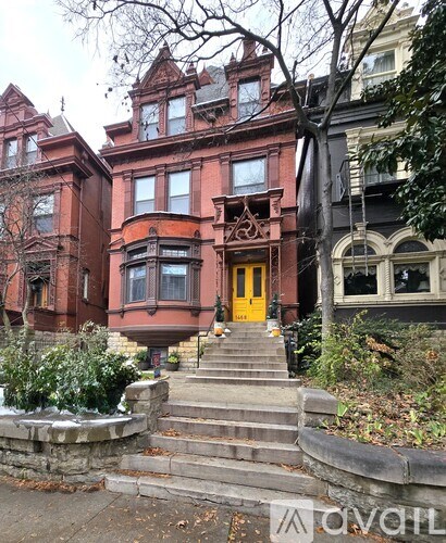 A red Victorian style house with a yellow door and steps leading up to it.