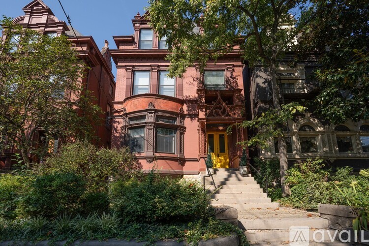 A red Victorian style house with a yellow door and stairs leading up to it.