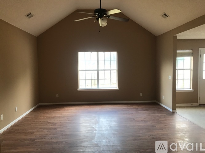 A spacious room with a ceiling fan and two windows.