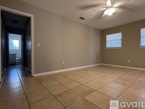 A spacious room with beige walls and tile flooring, featuring a ceiling fan and two windows.