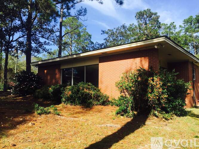 A house with a red brick exterior and a white roof is surrounded by trees and bushes.