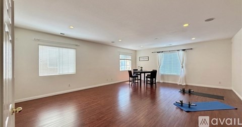 A yoga mat is placed on a wooden floor in a spacious room with a dining table and chairs.