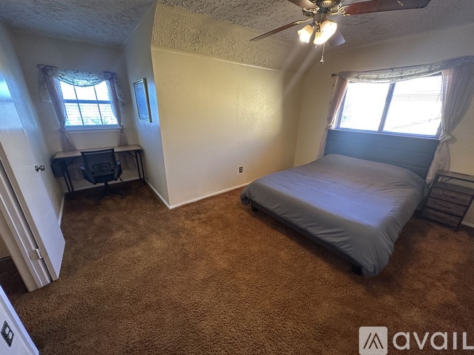 A bedroom with a bed, a desk, and a ceiling fan.