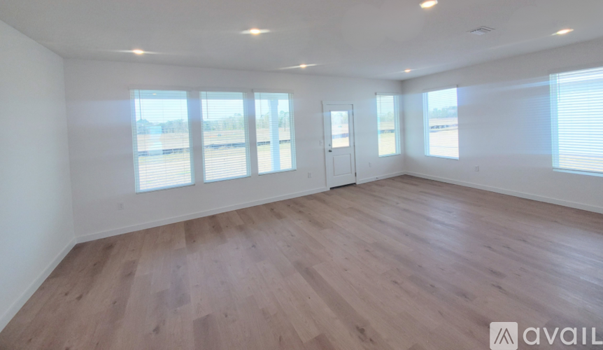 A spacious room with wooden flooring and large windows.
