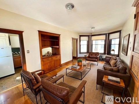 A living room with brown leather furniture and a kitchen in the background.