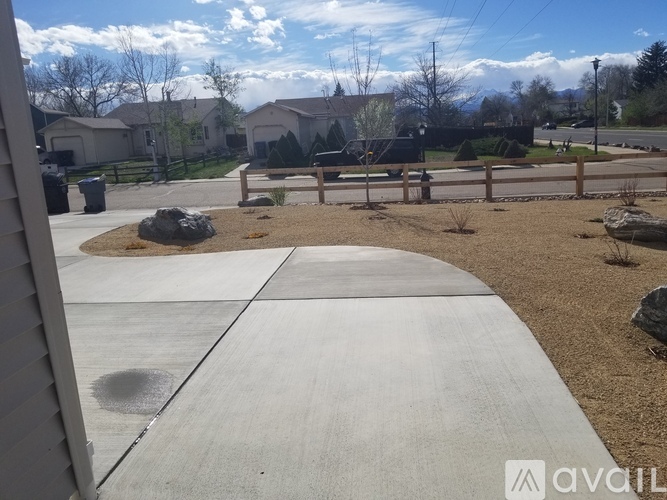 A concrete pathway leads through a landscaped area with a bench and a fence.
