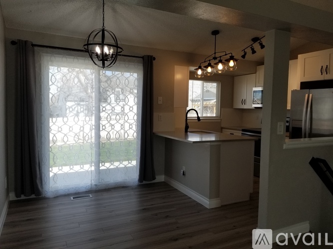 A kitchen with a wooden floor and a large window with curtains.