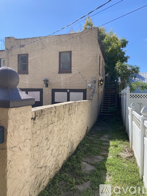 A narrow alley with a white fence on one side and a building with a stone wall on the other.