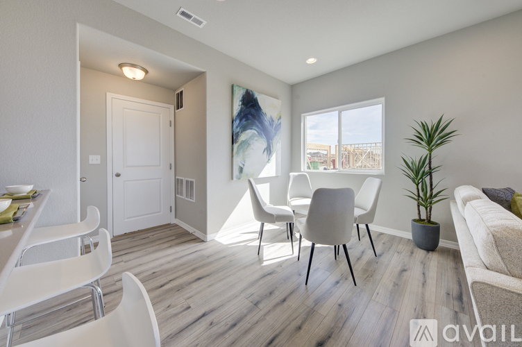 A living room with a white sofa, a dining table with chairs, and a plant.