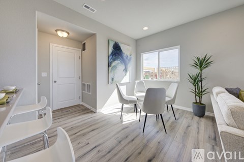 A living room with a white sofa, a dining table with chairs, and a plant.