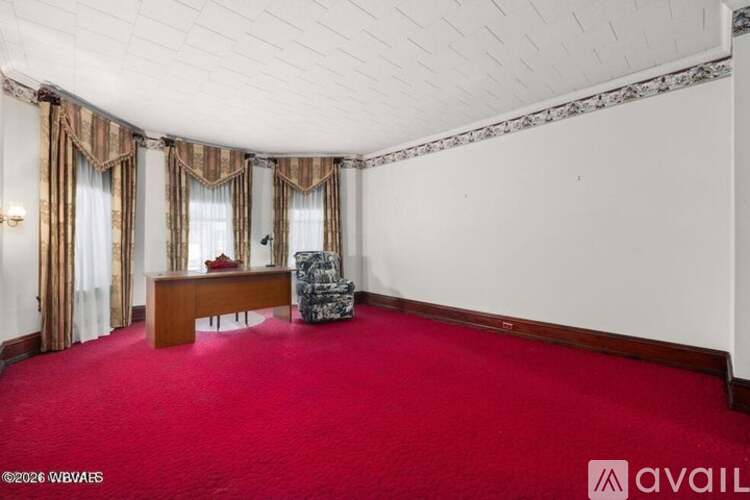 A room with a red carpet and a wooden desk with a chair.