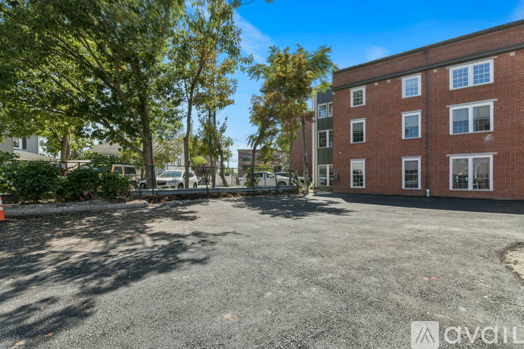 A parking lot in front of a red brick building with trees on the left side.