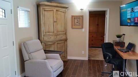 A room with a wooden cabinet, a grey recliner, and a black office chair.