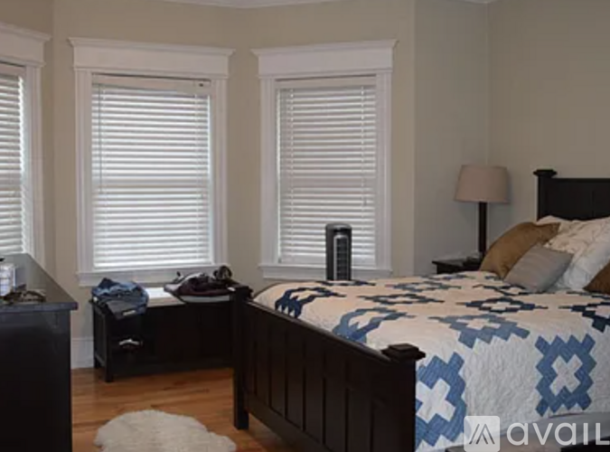 A bedroom with a bed, nightstand, and window with blinds.