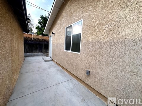A concrete patio leads to a door in a tan stucco building.