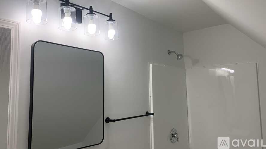 A bathroom with a mirror, light fixture, and shower.