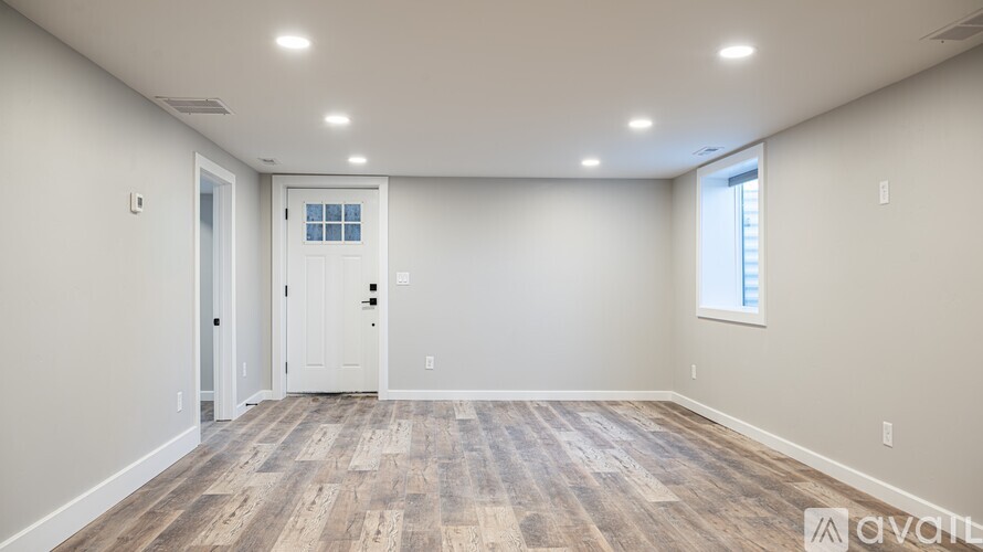 A spacious room with wooden flooring and a door on the left.