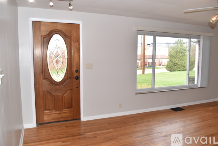 A room with a wooden door and a window showing a view of a lawn and a building outside.